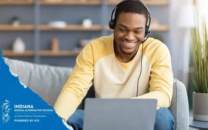 A smiling man in a yellow shirt and headphones sits on a couch, engaged with his laptop. On the left, there's text about Indiana Digital Alternative School.
